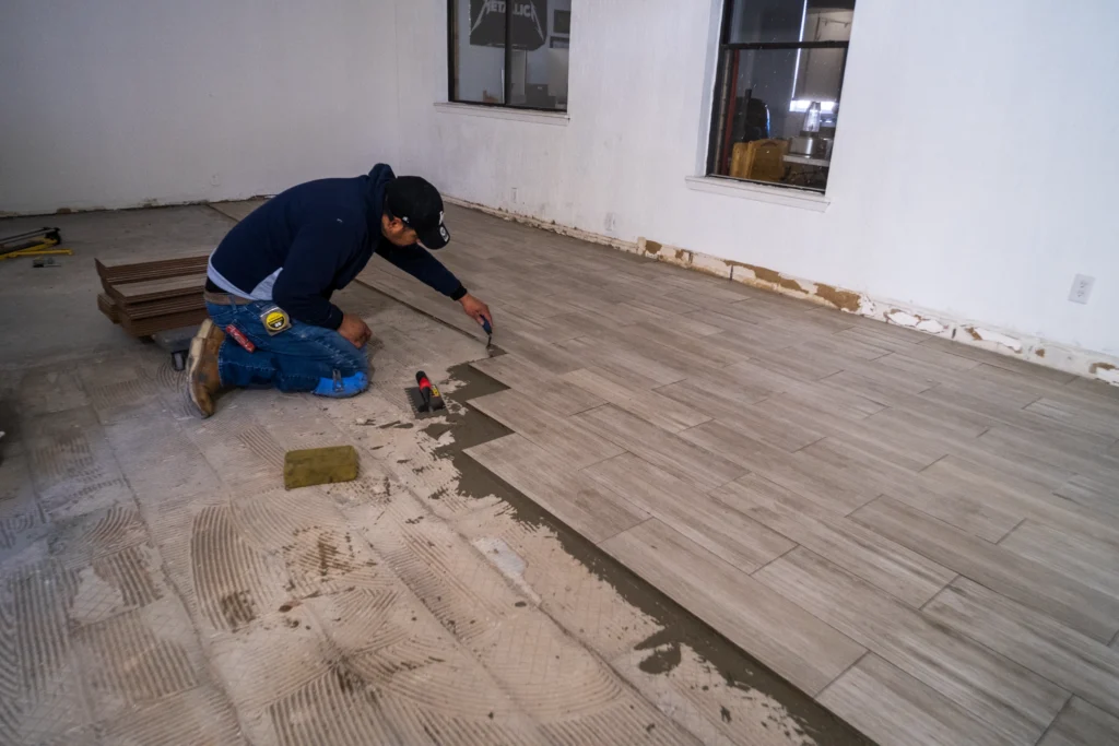 Flooring installer laying wood-look plank tile during a hard surface installation in El Paso, TX